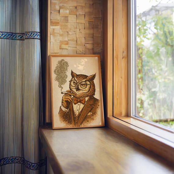 A framed print of an owl in a brown suit, red bow tie, and glasses, smoking a cigar with smoke curling up, sits on a wooden windowsill next to a striped curtain.