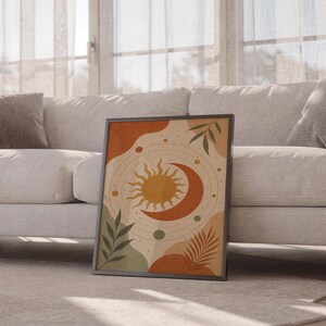 Celestial sun and moon art print leaning against a white sofa in a bright living room with sheer curtains.