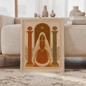 Terracotta arch and vase wall art print in a wood frame leaning against a cream sofa in a bright modern living room.