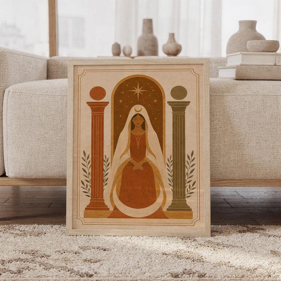 Terracotta arch and vase wall art print in a wood frame leaning against a cream sofa in a bright modern living room.