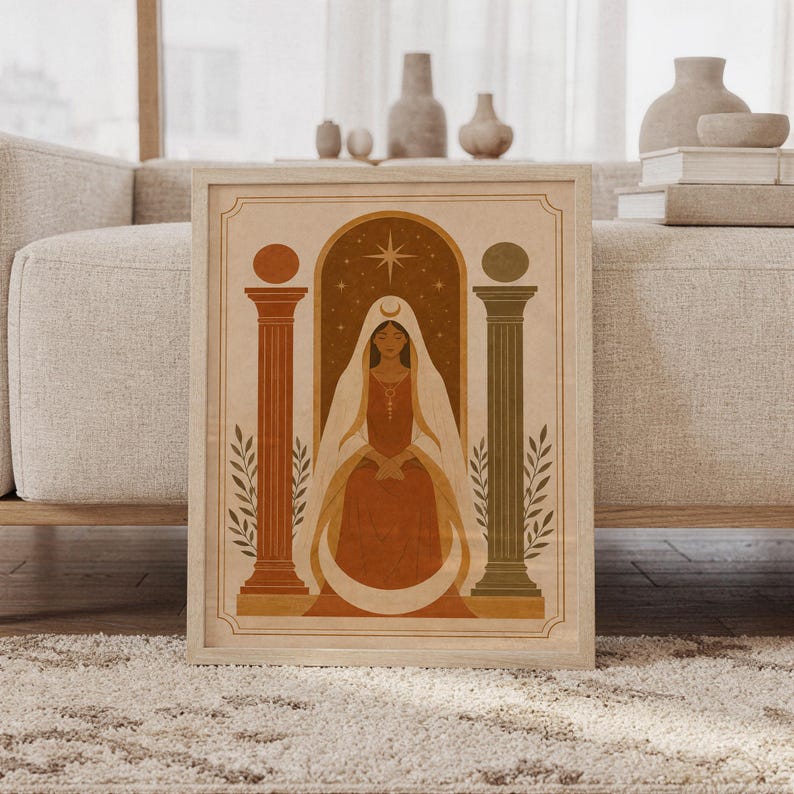 Terracotta arch and vase wall art print in a wood frame leaning against a cream sofa in a bright modern living room.