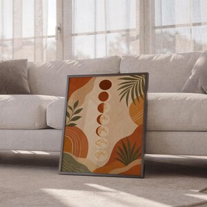 Boho moon phases art print leaning against a white sofa in a bright living room with sheer curtains.