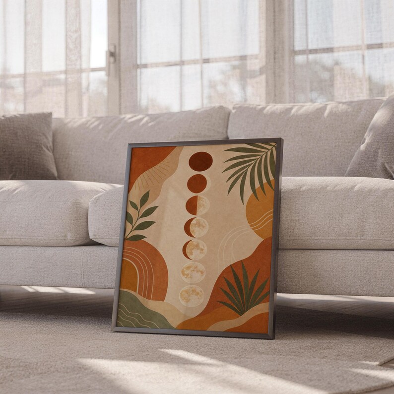 Boho moon phases art print leaning against a white sofa in a bright living room with sheer curtains.