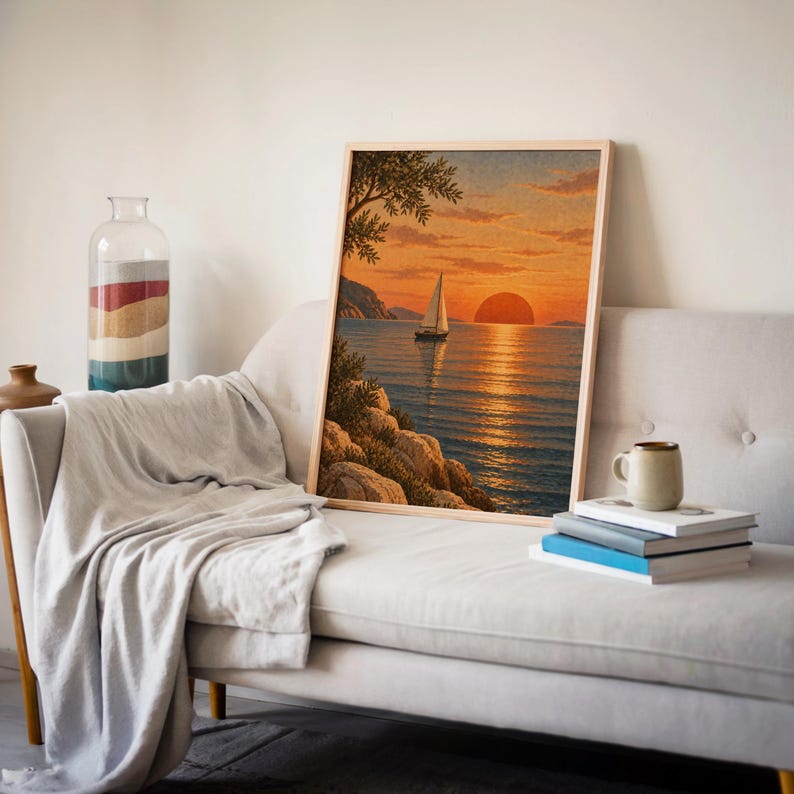Sunset sailboat wall art print leaning on a cream sofa against a beige wall beside books and a mug.