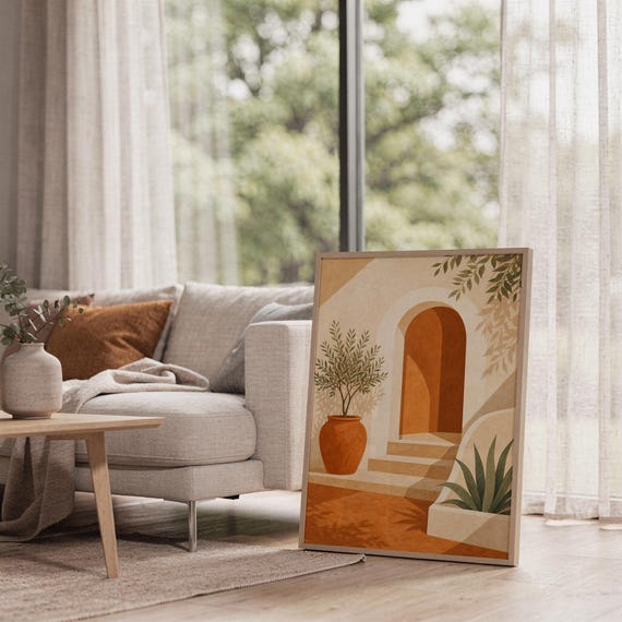 Mediterranean terracotta stairway arch print leaning on the floor beside a cream armchair next to large garden windows.
