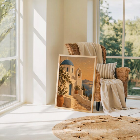 Santorini church wall art print leaning on the floor beside a rattan armchair and jute rug in a bright sunlit room.