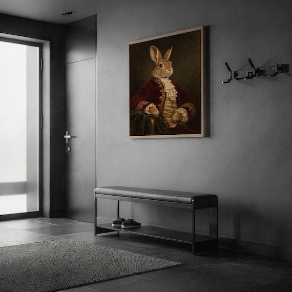 Regal rabbit portrait wall art print in a silver frame leaning against a sofa beside a decorative marble sphere.