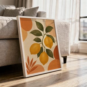 Lemon branch botanical print in a white frame leaning against a gray sofa on a sunlit wooden floor.