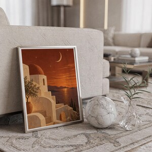 Mediterranean moonlit coastal wall art print in a silver frame leaning against a sofa beside a decorative marble sphere.