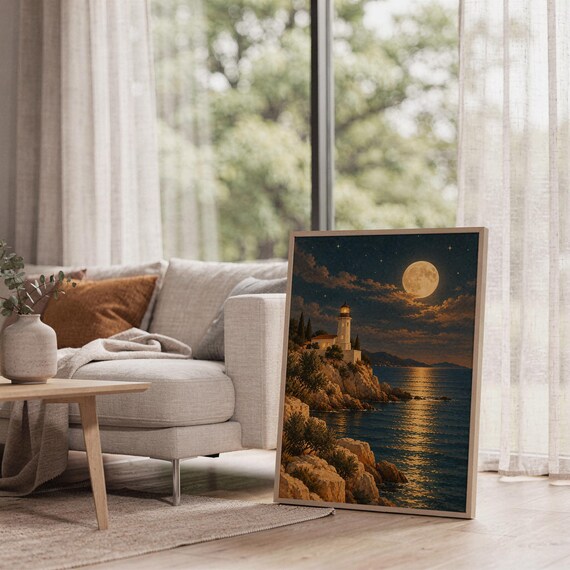 Moonlit lighthouse wall art print leaning on the floor beside a cream armchair next to large garden windows.