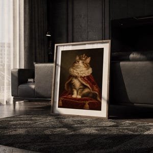 Royal cat portrait wall art print leaning on the floor beside a cream armchair next to large garden windows.