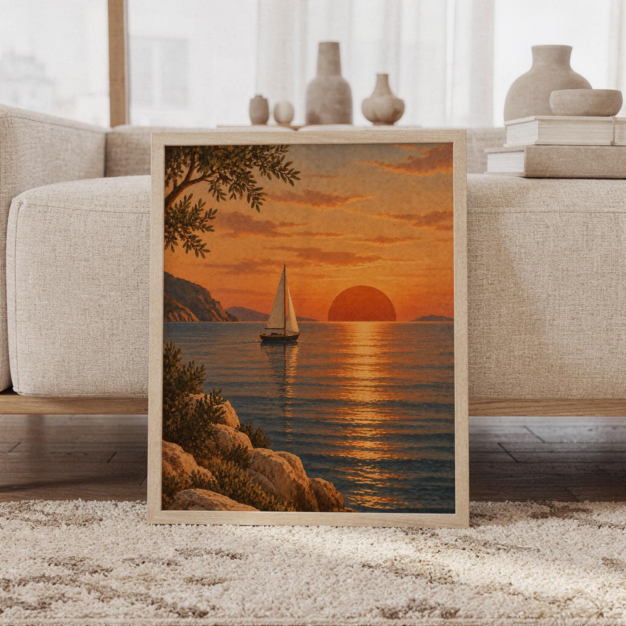 Sunset sailboat wall art print featuring glowing burnt orange, golden ochre, muted blue water, rocky shores, leafy branches, and a lone sailboat beneath a setting sun, framed and leaning against a beige sofa on a textured rug in a bright Scandinavian living room.