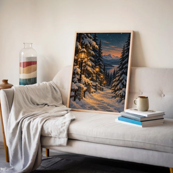 Snowy forest path wall art print leaning on a cream sofa against a beige wall beside books and a mug.