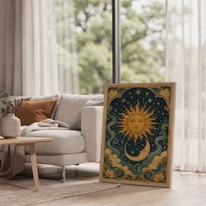 Celestial sun and moon wall art print leaning on the floor beside a cream armchair next to large garden windows.