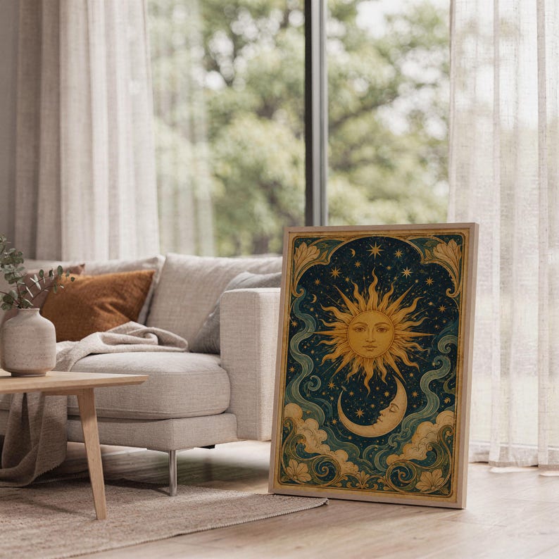 Celestial sun and moon wall art print leaning on the floor beside a cream armchair next to large garden windows.
