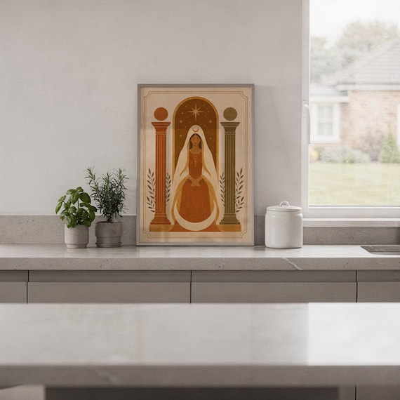 Modern boho arch artwork in a frame placed on a sleek white kitchen countertop next to potted indoor herbs.