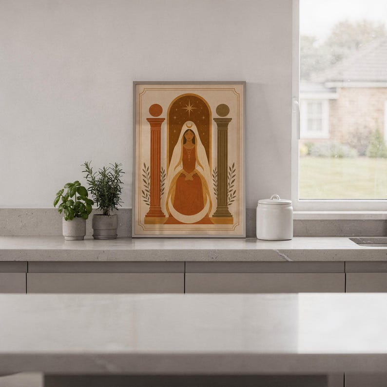 Modern boho arch artwork in a frame placed on a sleek white kitchen countertop next to potted indoor herbs.