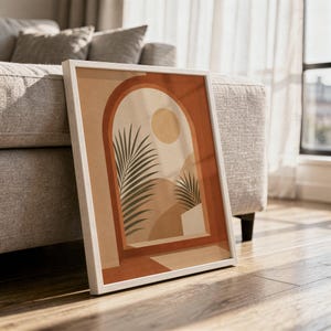 Large framed terracotta arch window poster on hardwood floor leaning next to sofa in sunlit room.