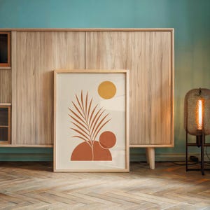 Terracotta palm leaf print leaning against light wooden sideboard cabinet