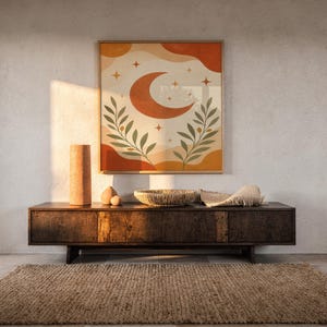Terracotta crescent moon and olive branch print hanging above a dark wood console and jute rug in a warm neutral interior.