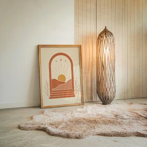 Large desert sun wall art resting on floor beside modern woven floor lamp