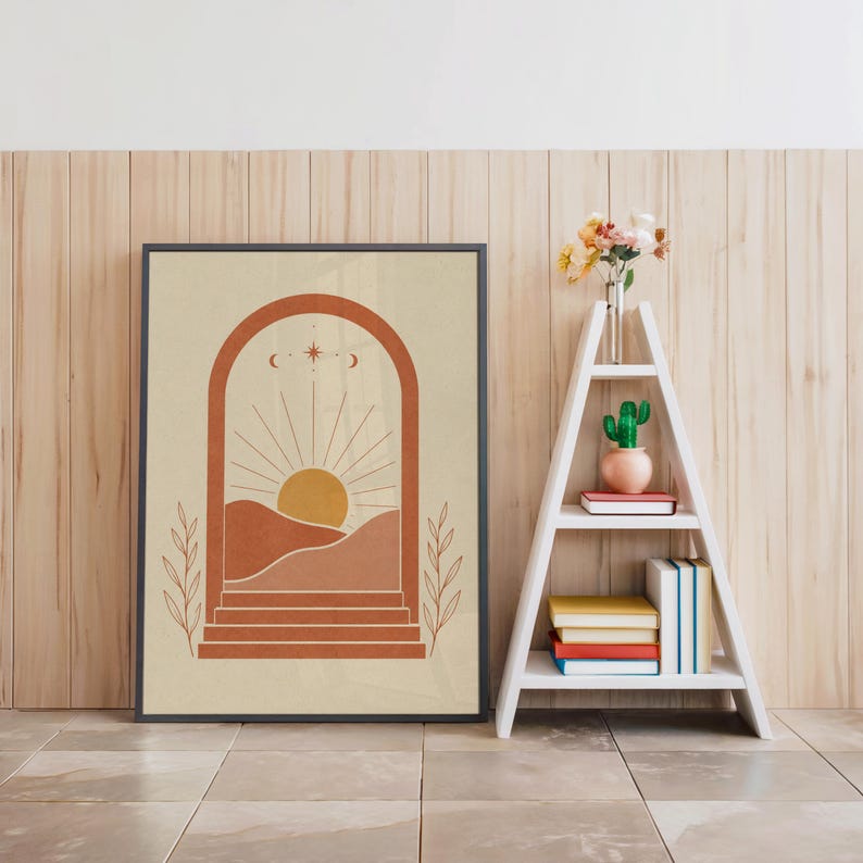 Desert sun wall art in black frame resting on floor beside decorative white ladder shelf