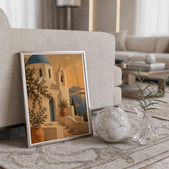 Santorini church wall art print in a silver frame leaning against a sofa beside a decorative marble sphere.