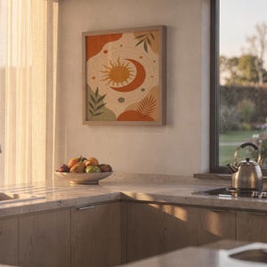 Celestial sun and moon art print hanging above a stone countertop with a fruit bowl in a sunny kitchen.
