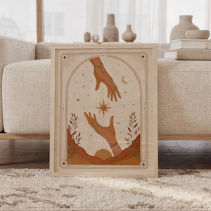 Framed mystical celestial hands tarot art print leaning on carpet in front of sofa in bright living room.