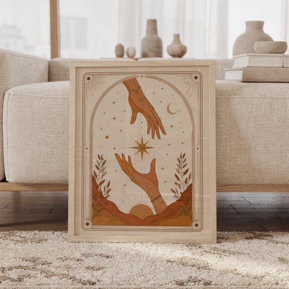 Framed mystical celestial hands tarot art print leaning on carpet in front of sofa in bright living room.