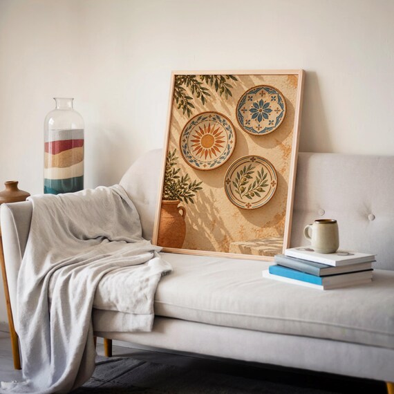 Mediterranean ceramic plate wall art print leaning on a cream sofa against a beige wall beside books and a mug.