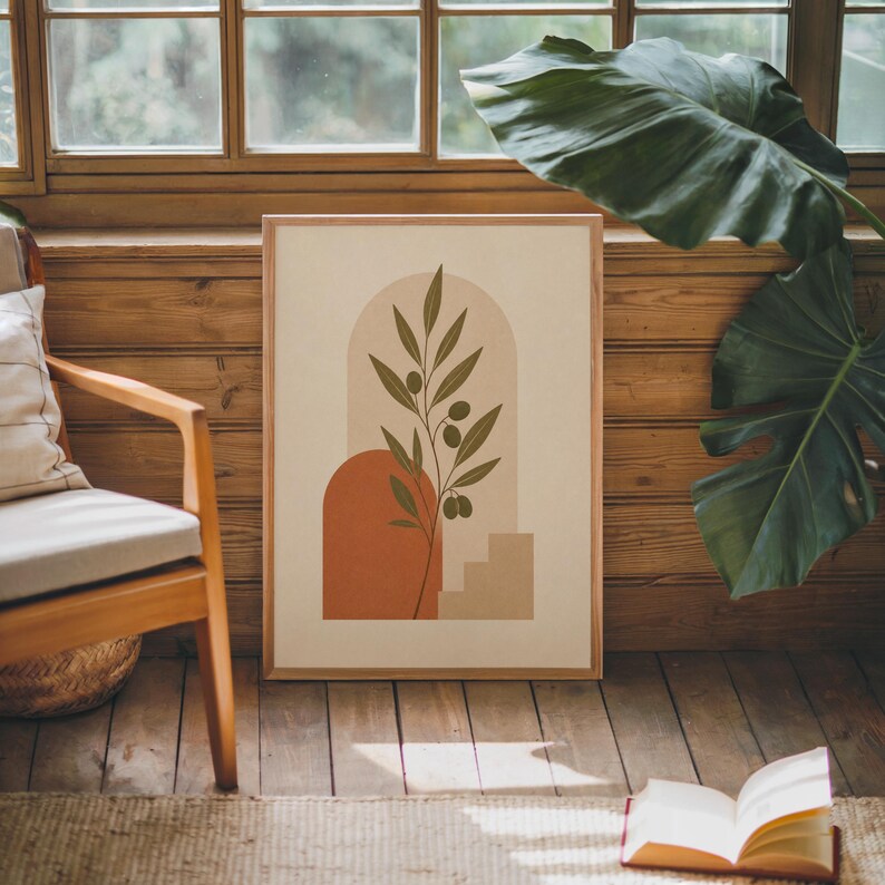 Single framed terracotta arch leaf print resting on a wooden floor next to a green houseplant.