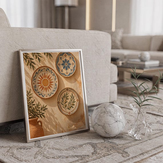 Mediterranean ceramic plate wall art print in a silver frame leaning against a sofa beside a decorative marble sphere.
