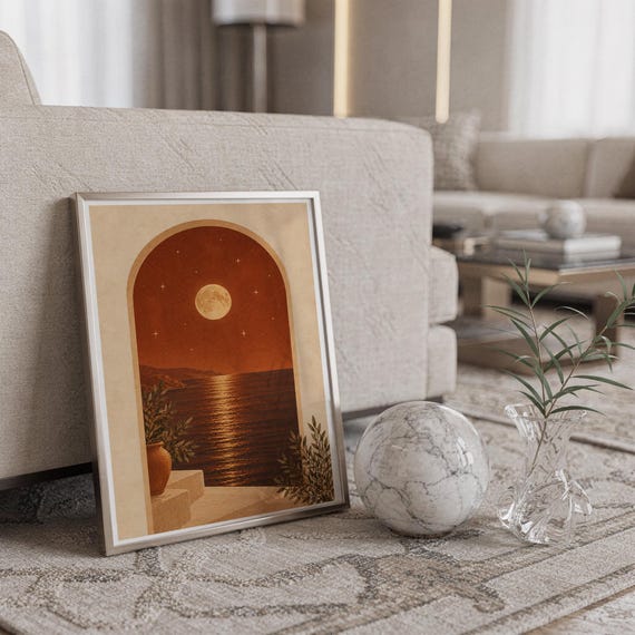 Moonlit Mediterranean arch print in a silver frame leaning against a sofa beside a decorative marble sphere.
