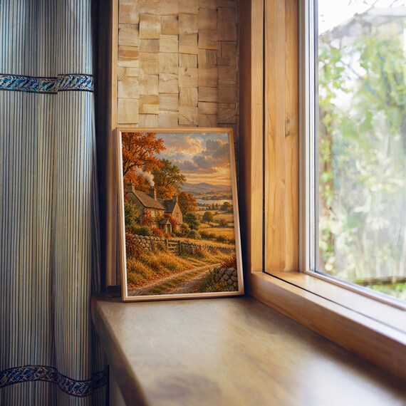 Autumn cottage landscape wall art print standing on a wooden window sill in warm natural light.