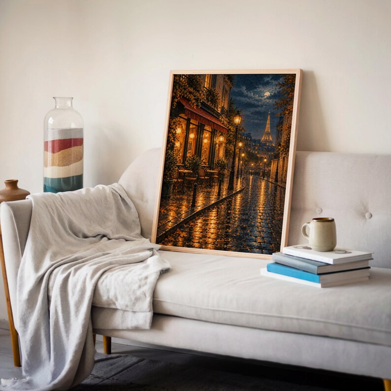 Paris eiffel tower wall art print leaning on a cream sofa against a beige wall beside books and a mug.