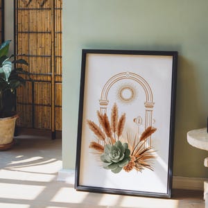 Celestial pampas grass and sage green succulent wall art print framed in a sleek black frame set on the floor against a muted sage green accent wall beside modern decorative glass bottles and stool decor.