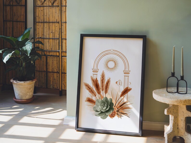 Celestial pampas grass and sage green succulent wall art print framed in a sleek black frame set on the floor against a muted sage green accent wall beside modern decorative glass bottles and stool decor.