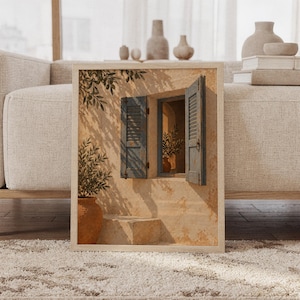 Mediterranean blue shutter wall art print featuring sun-washed cream stone, weathered blue shutters, terracotta pottery, and leafy olive branches in a rustic Mediterranean style, framed and leaning against a beige sofa on a textured rug in a bright Scandinavian living room.