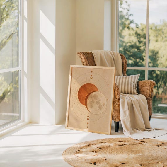 Sun and moon celestial wall art print leaning on the floor beside a rattan armchair and jute rug in a bright sunlit room.