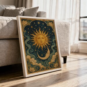 Celestial sun and moon wall art print in a white frame leaning against a gray sofa on a sunlit wooden floor.