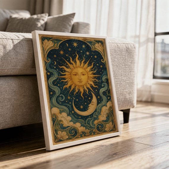 Celestial sun and moon wall art print in a white frame leaning against a gray sofa on a sunlit wooden floor.