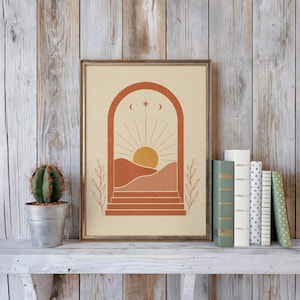Single abstract terracotta sun arch poster from the set of 3 framed in light wood resting on a rustic shelf alongside stacked hardcover books and a potted cactus plant with natural daylight.