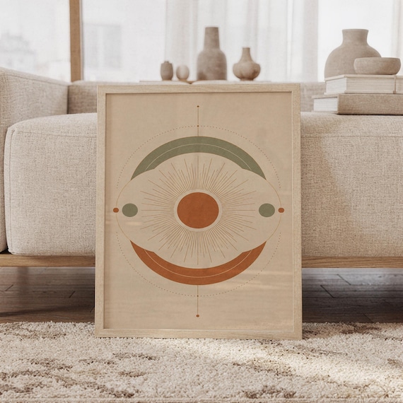 Abstract sun wall art print featuring warm terracotta, muted sage green, and soft cream tones with a radiant sunburst and layered geometric circles, framed and leaning against a beige sofa on a textured rug in a bright Scandinavian living room.