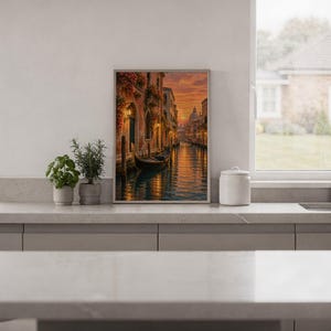 Venice canal sunset wall art print standing on a white kitchen counter beside potted herbs.
