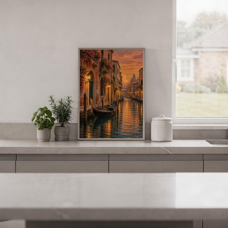 Venice canal sunset wall art print standing on a white kitchen counter beside potted herbs.