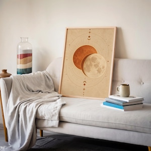 Sun and moon celestial wall art print leaning on a cream sofa against a beige wall beside books and a mug.