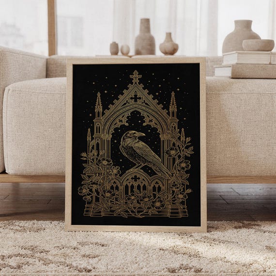 Gothic raven wall art print featuring a black backdrop, intricate antique gold linework, a regal raven beneath an ornate cathedral arch, scattered stars, and climbing florals, framed and leaning against a beige sofa on a textured rug in a bright Scandinavian living room.