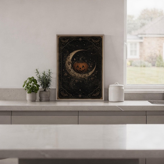 Vintage halloween moon wall art print standing on a white kitchen counter beside potted herbs.