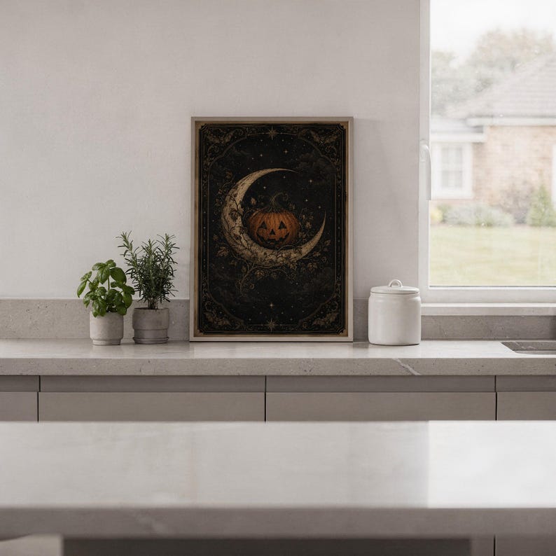 Vintage halloween moon wall art print standing on a white kitchen counter beside potted herbs.